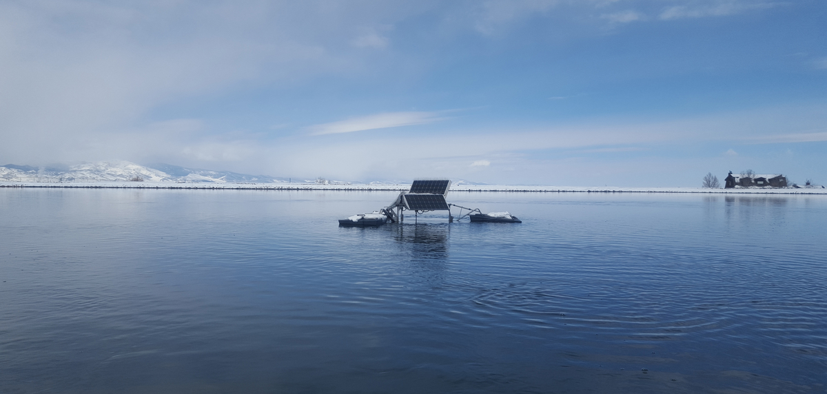 SolarBee® lake mixer in a winter, icy blue lake with snow and cabin in the background